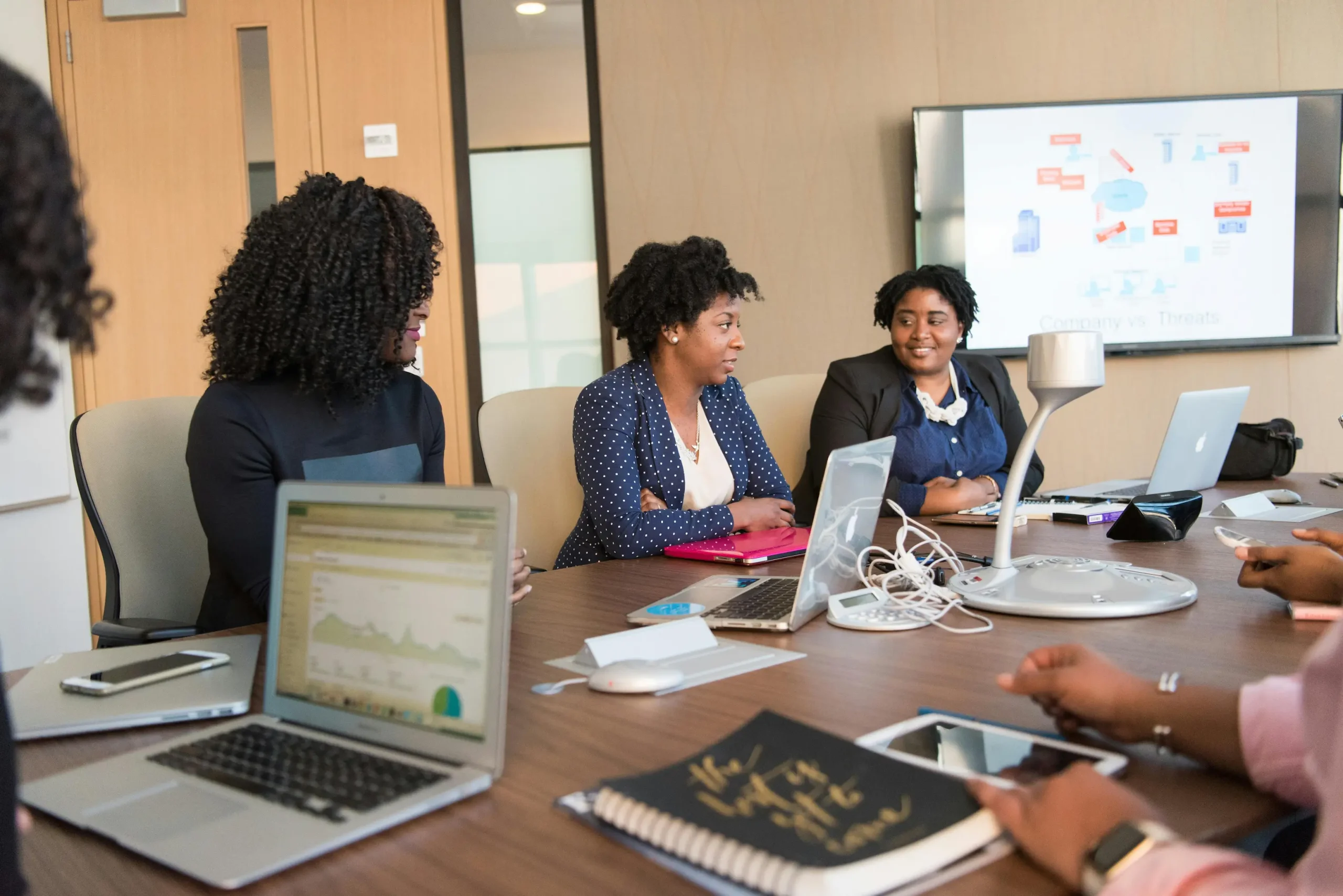 Community association management team discussing strategy during a boardroom meeting with laptops and presentation screen.