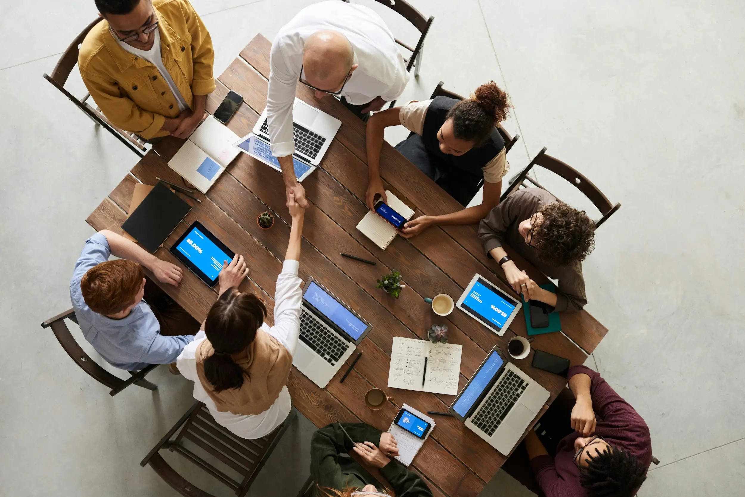 Community association management team collaborating around a table with laptops and tablets during a planning meeting.