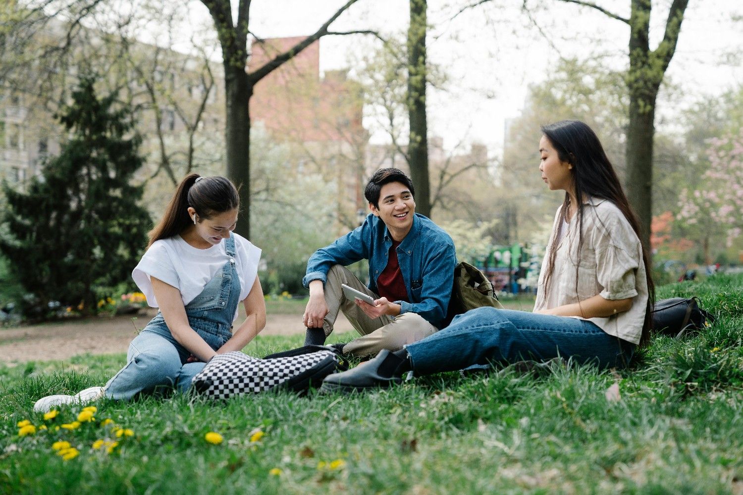 Three young adults sitting together on grass in a park, representing resident connection and community engagement in a master-planned community.