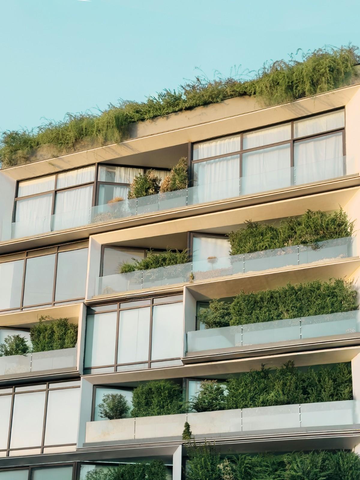 Contemporary condominium building with glass balconies, large windows, and integrated greenery managed by a condo association