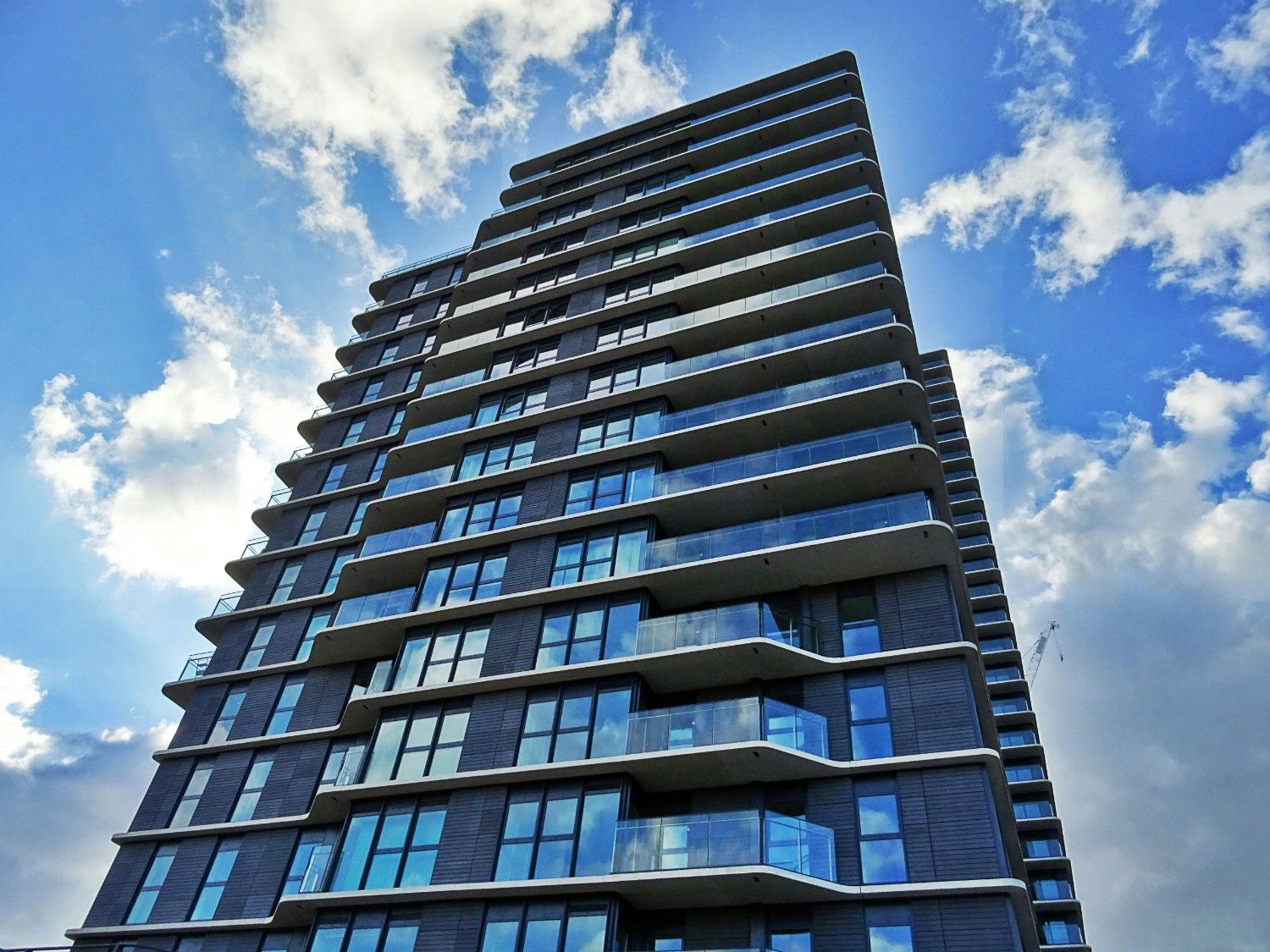 Modern residential high-rise with balconies viewed from below, representing multifamily housing in a master-planned community.