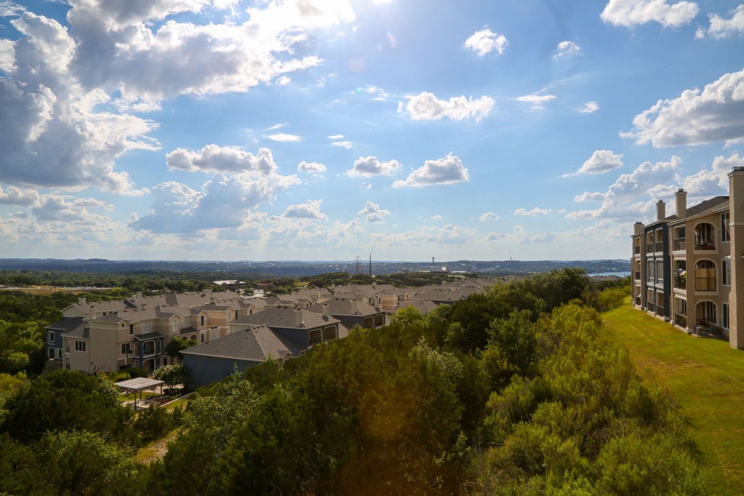 Landscaped residential condominium community with green lawns, mature trees, and mid-rise buildings under a blue sky.